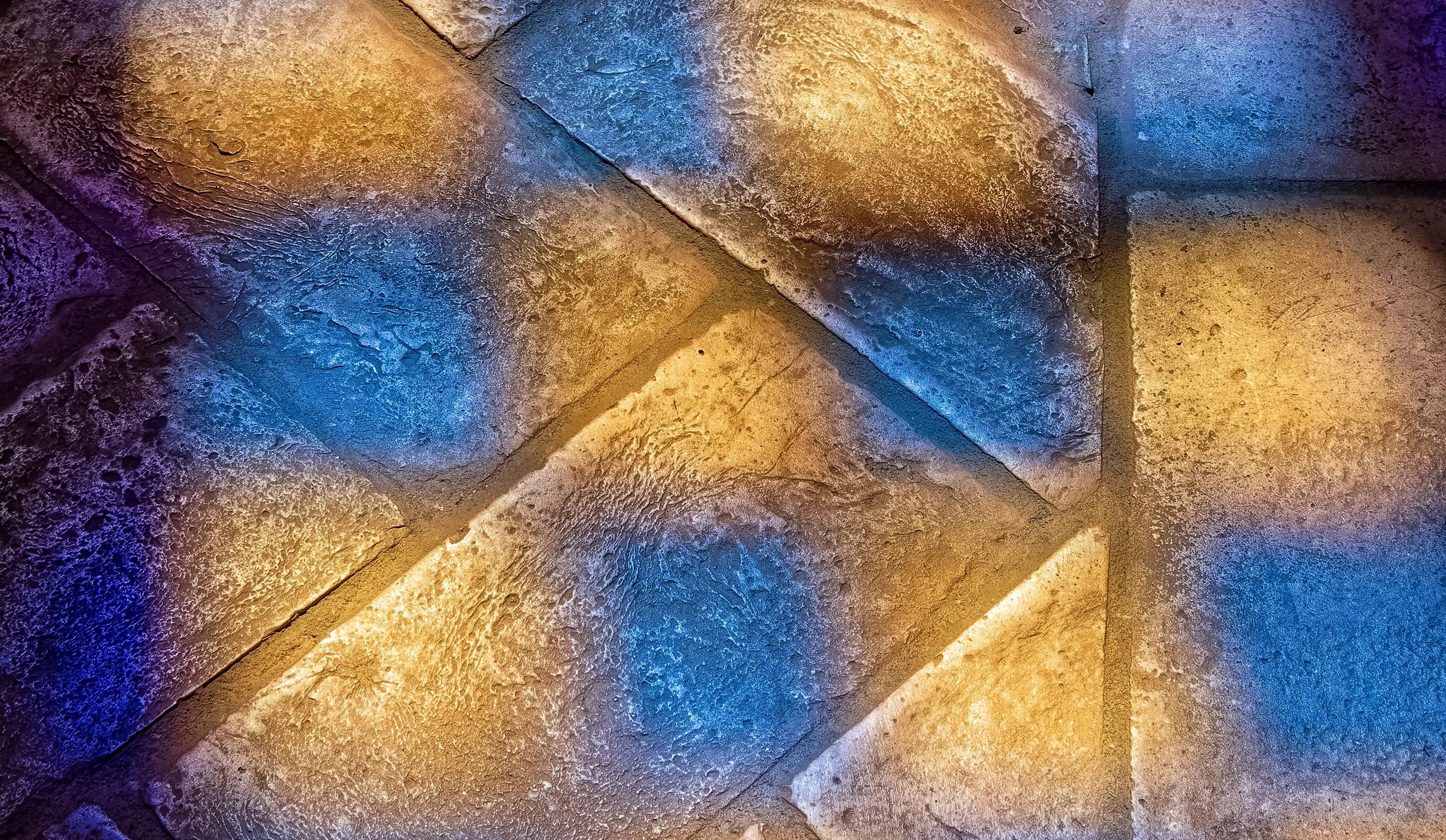 Texturierte Steinfliesen, die mit farbigem blauem und bernsteinfarbenem Licht beleuchtet werden und ein geometrisches Muster bilden.